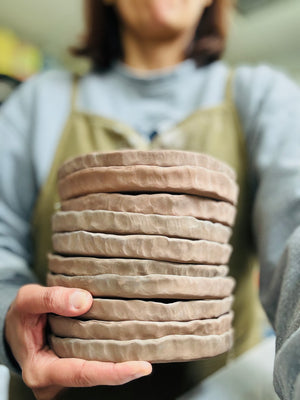 Stack of round, beige coasters held by a person wearing a gray shirt and green apron.
