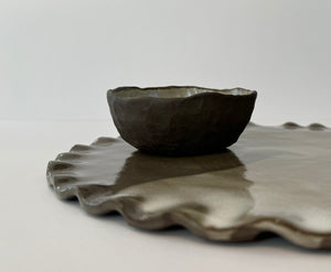 Ceramic bowl on a matching ceramic tray with scalloped edges against a white background