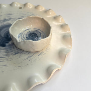 side view of a bowl on a ceramic platter with scalloped edges on white base and grey background