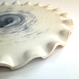 Side view of a ceramic platter with scalloped edges on white base and grey background