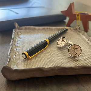 Pen and cufflinks on a textured surface with a blurred background
